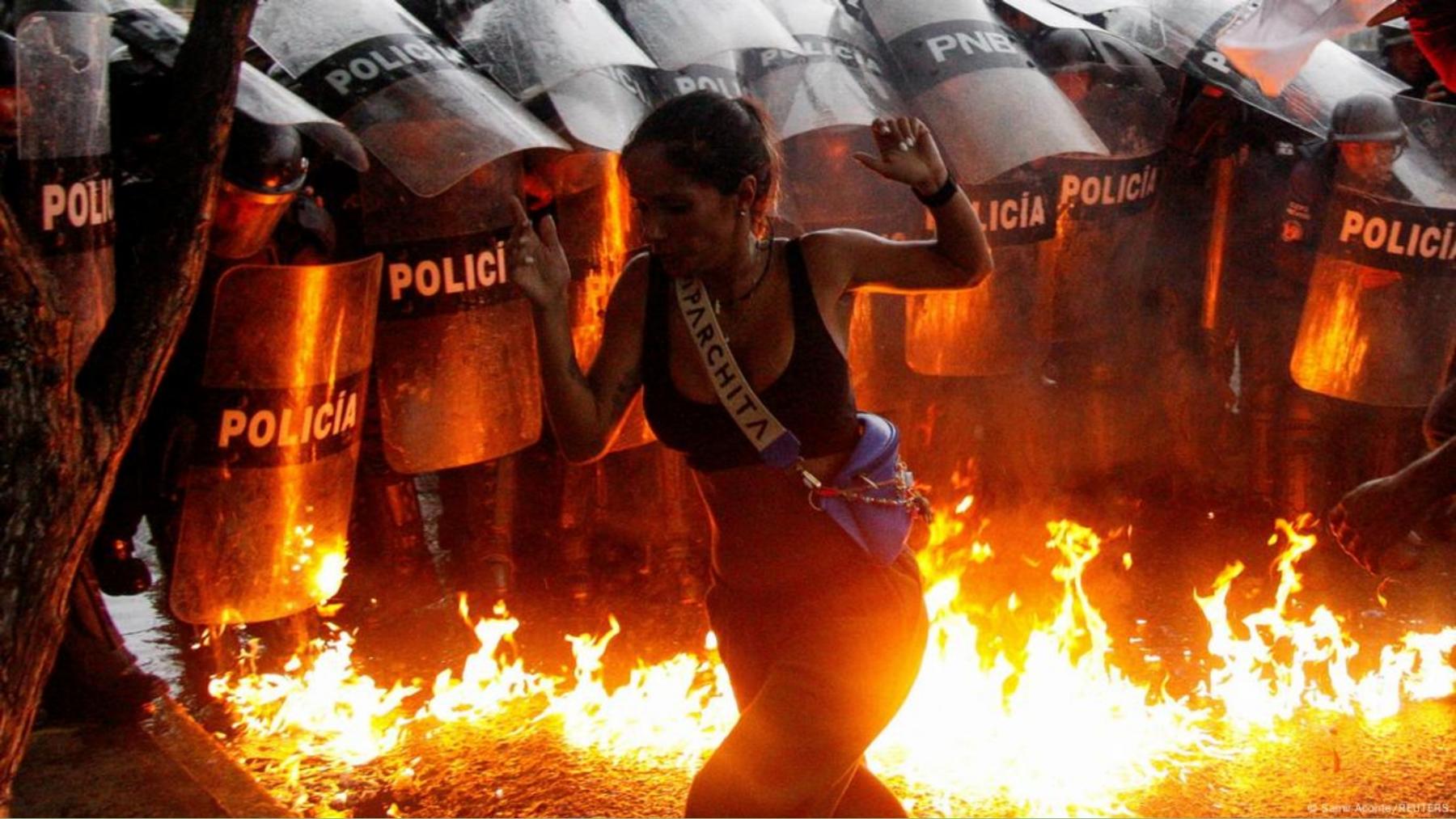 Una mujer camina cerca de las llamas causadas por una bomba molotov en Puerto La Cruz